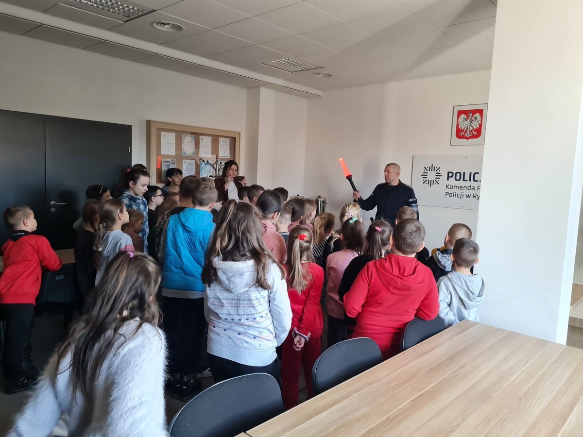 Na zdjęciu widać grupę dzieci z przedszkola i klas I-III z Grabowa Szlacheckiego które na sali odpraw maja prezentowane przez policjanta wyposażenie policyjne