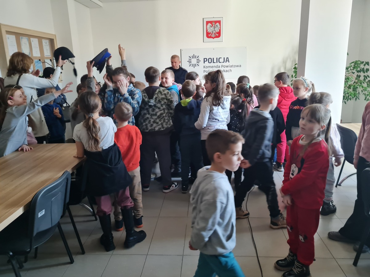 Na zdjęciu widać grupę dzieci z przedszkola i klas I-III z Grabowa Szlacheckiego które na sali odpraw maja prezentowane przez policjanta wyposażenie policyjne