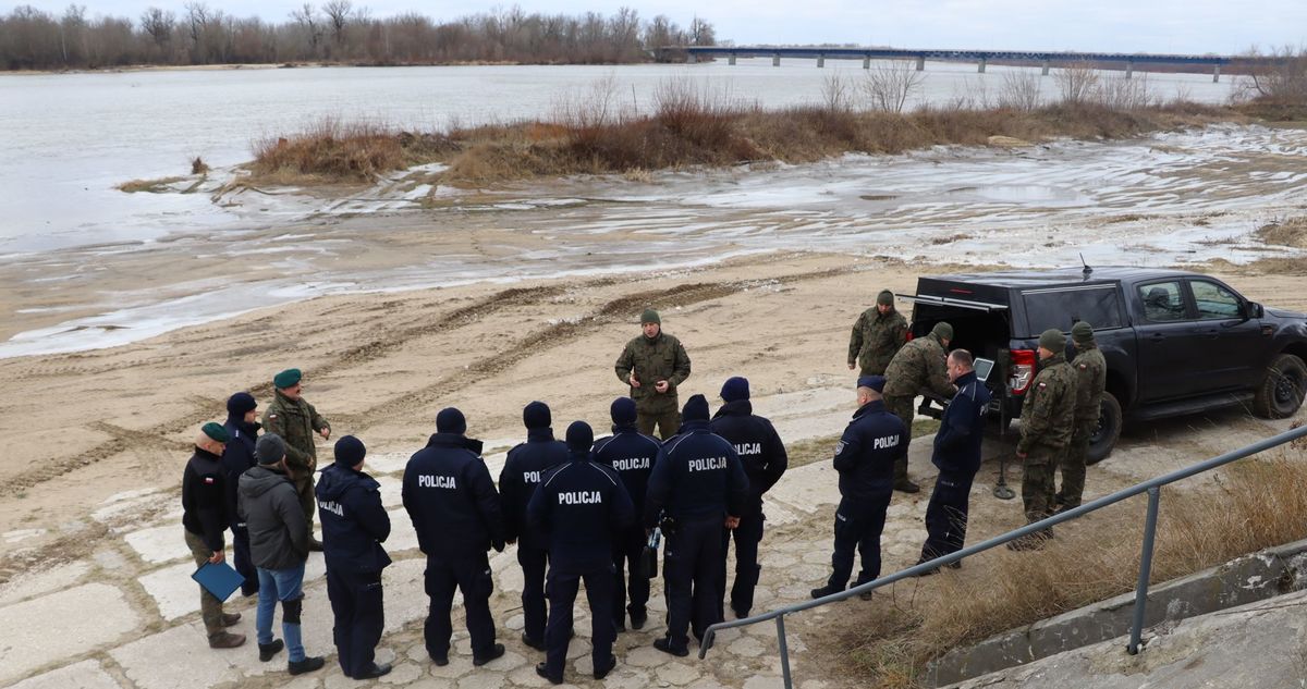 Zdjęcie przedstawia funkcjonariuszy policji oraz żołnierzy stojacych nad brzegiem rzeki Wisły gdzie prezentowany jest wykorzystywany sprzęt przez saperów